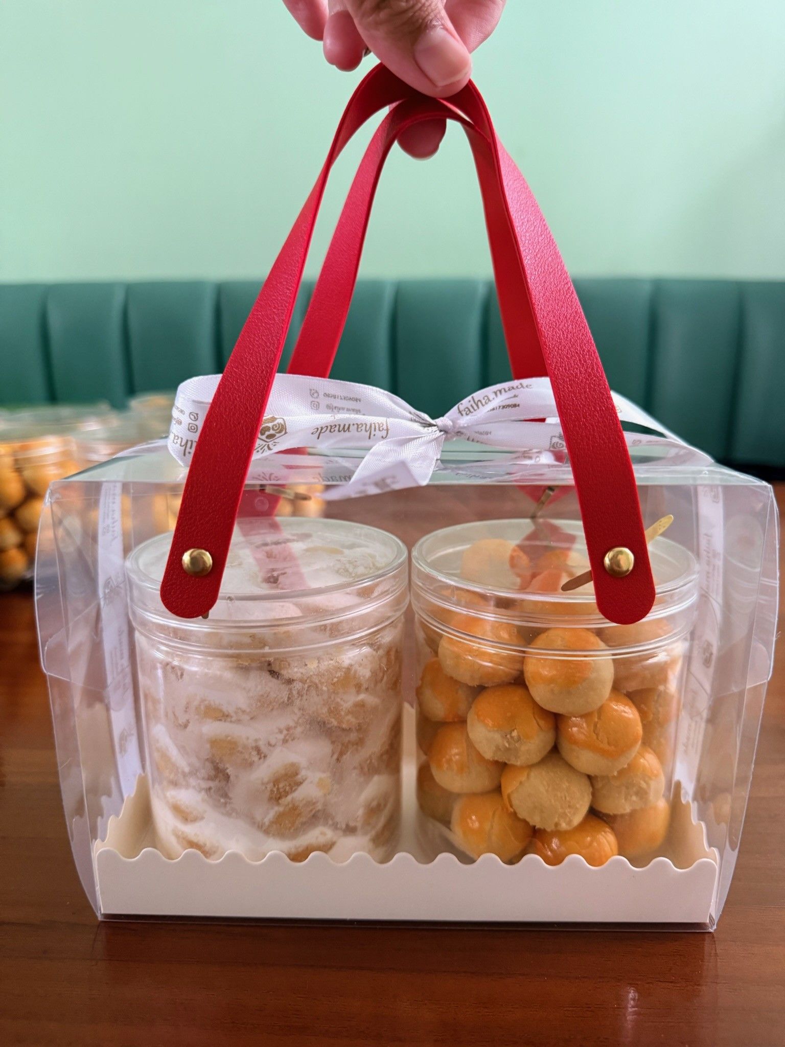 Tangan mengangkat hampers dua toples nastar dan putri salju berhandle merah, kue faiha.id untuk ulang tahun di kantor